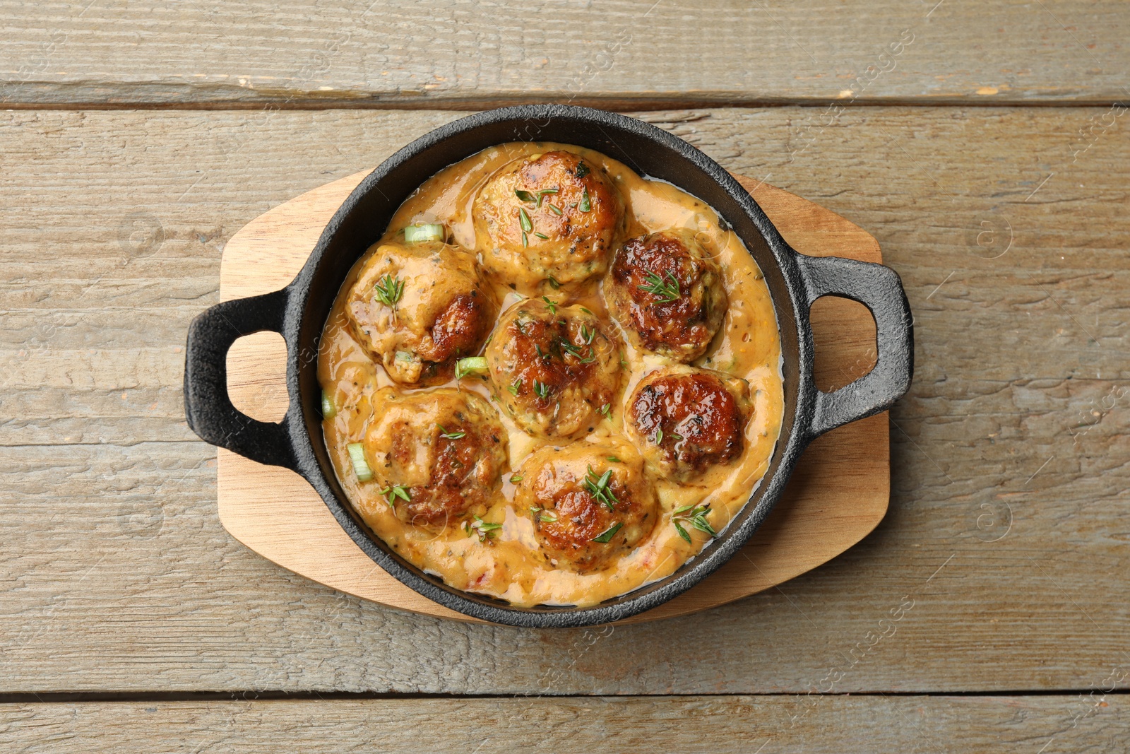 Photo of Delicious meatballs with gravy cream sauce and herbs on wooden table, top view