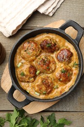 Photo of Delicious meatballs with gravy cream sauce and herbs on wooden table, flat lay