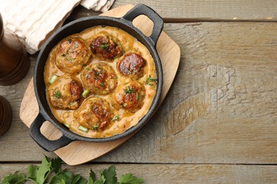 Photo of Delicious meatballs with gravy cream sauce and herbs on wooden table, flat lay. Space for text