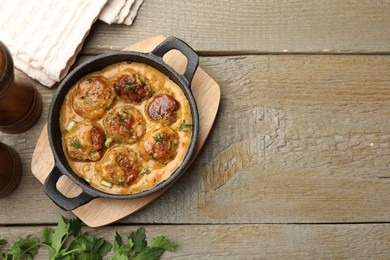 Photo of Delicious meatballs with gravy cream sauce and herbs on wooden table, flat lay. Space for text