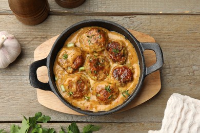 Photo of Delicious meatballs with gravy cream sauce and herbs on wooden table, flat lay