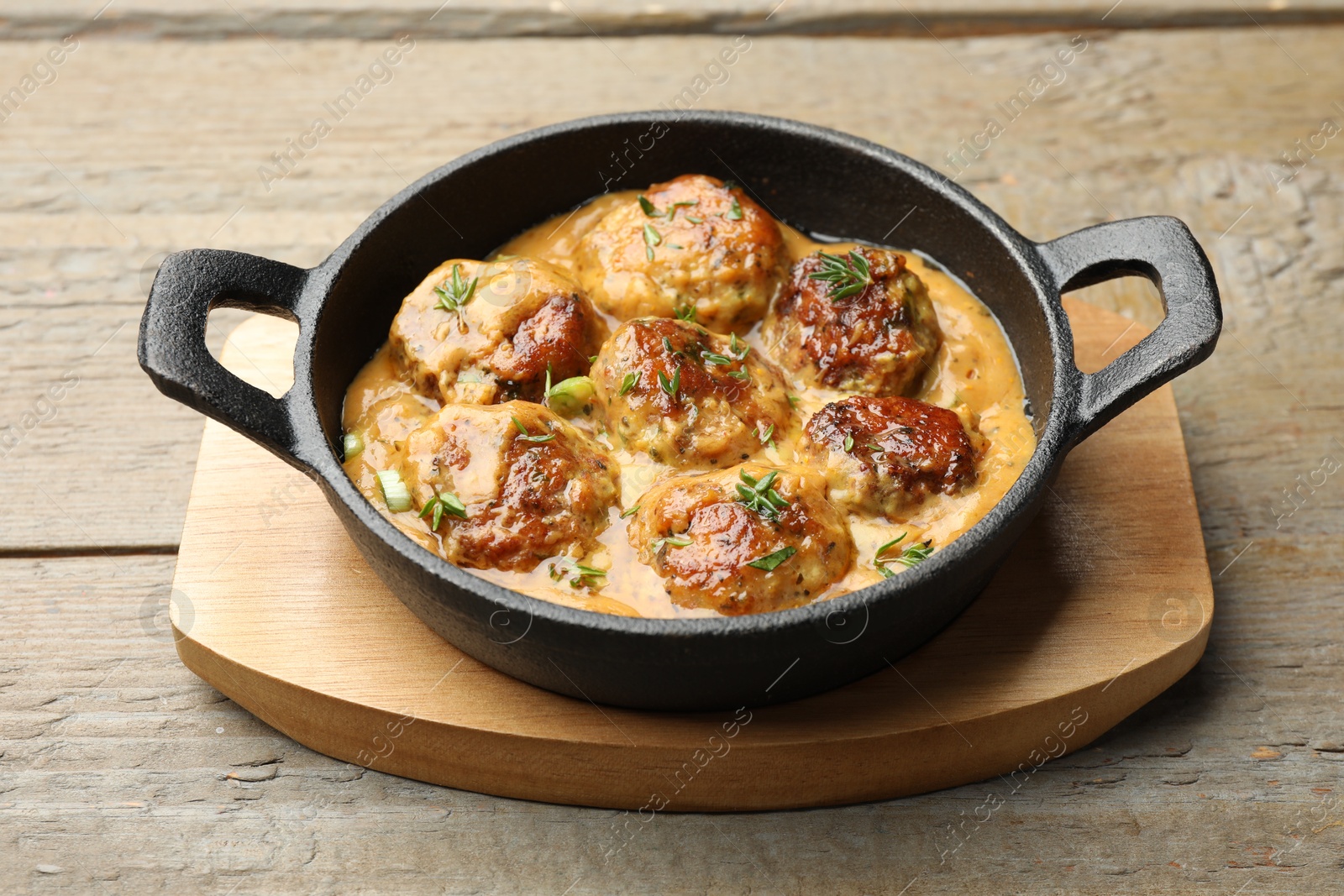 Photo of Delicious meatballs with gravy cream sauce and herbs on wooden table, closeup