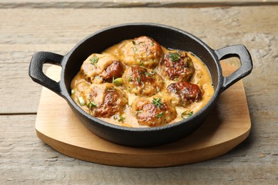 Photo of Delicious meatballs with gravy cream sauce and herbs on wooden table, closeup