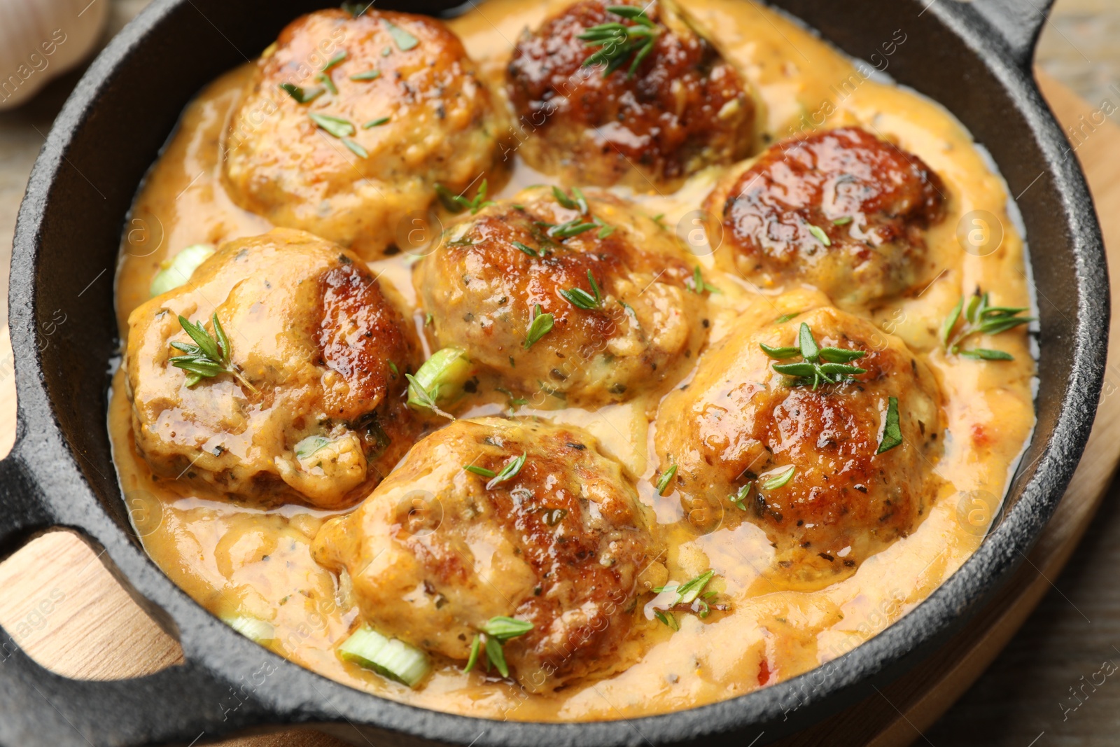 Photo of Delicious meatballs with gravy cream sauce and herbs on wooden table, closeup