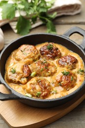 Photo of Delicious meatballs with gravy cream sauce and herbs on wooden table, closeup