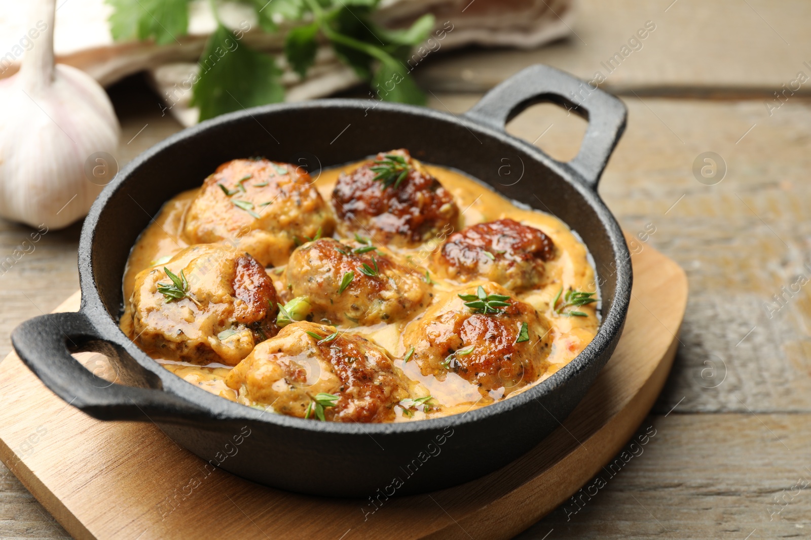 Photo of Delicious meatballs with gravy cream sauce and herbs on wooden table, closeup