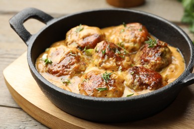 Photo of Delicious meatballs with gravy cream sauce and herbs on wooden table, closeup