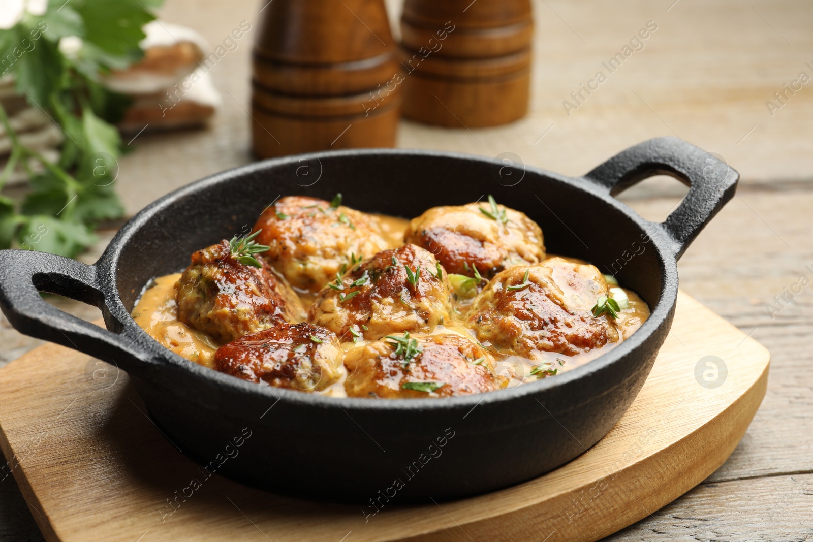 Photo of Delicious meatballs with gravy cream sauce and herbs on wooden table, closeup