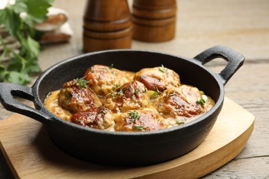 Photo of Delicious meatballs with gravy cream sauce and herbs on wooden table, closeup