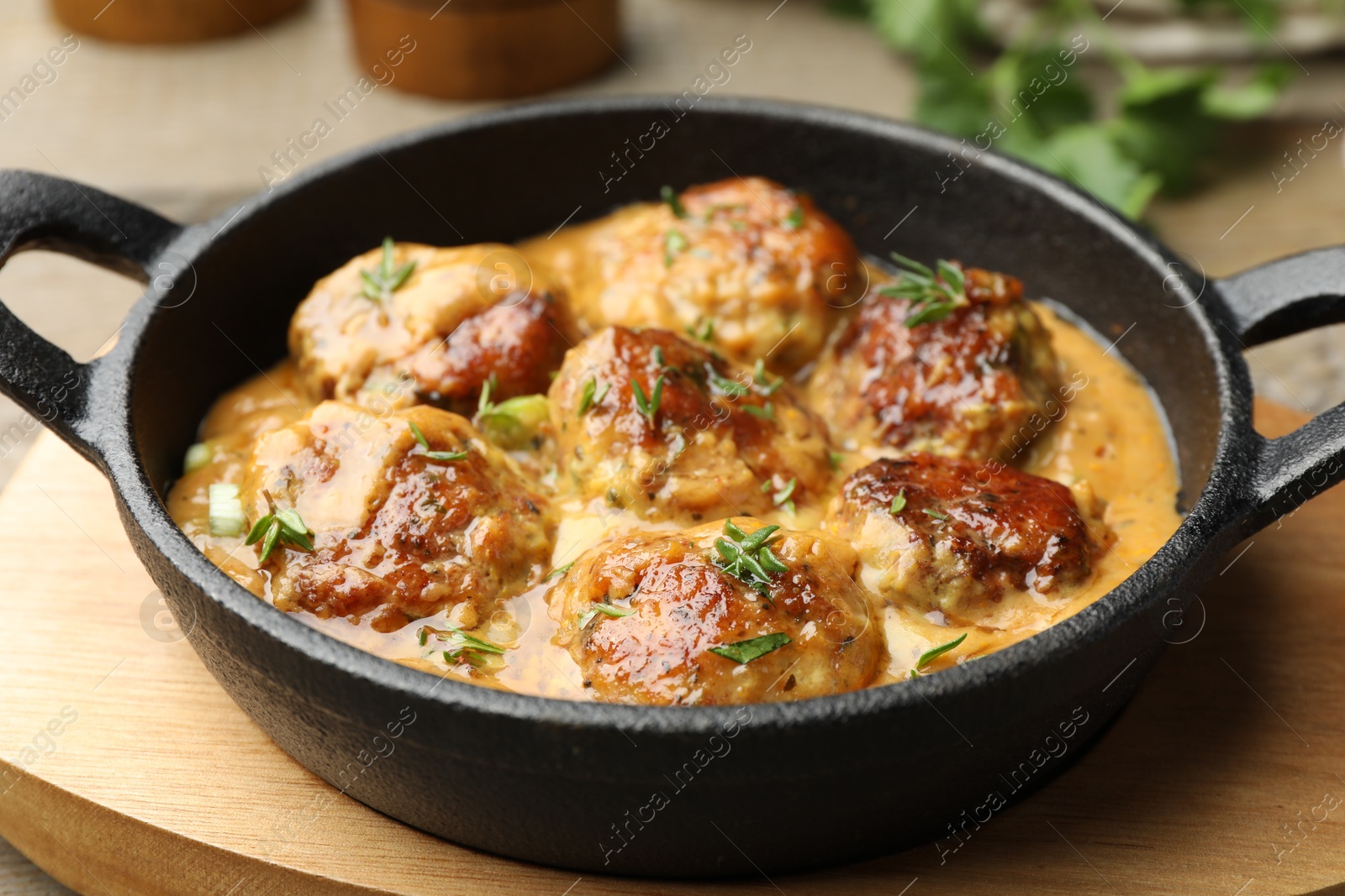 Photo of Delicious meatballs with gravy cream sauce and herbs on wooden table, closeup