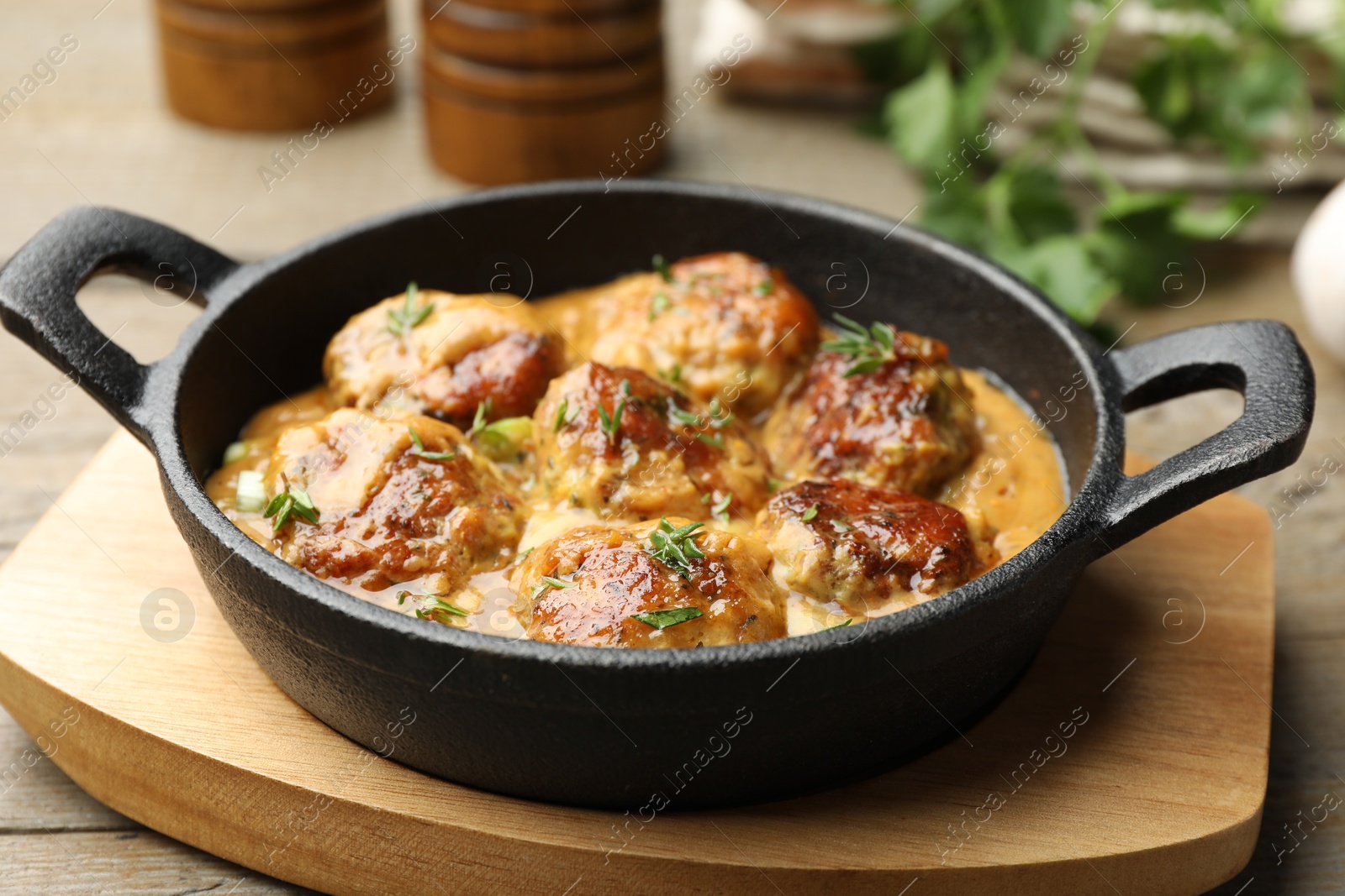 Photo of Delicious meatballs with gravy cream sauce and herbs on wooden table, closeup