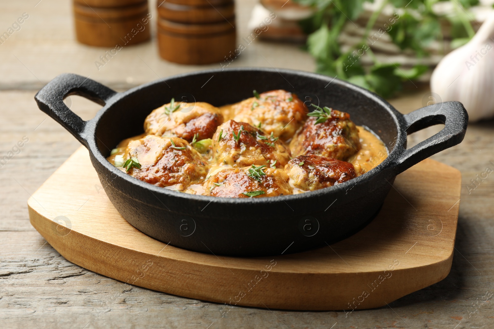 Photo of Delicious meatballs with gravy cream sauce and herbs on wooden table, closeup