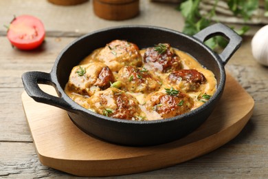 Photo of Delicious meatballs with gravy cream sauce and herbs on wooden table, closeup