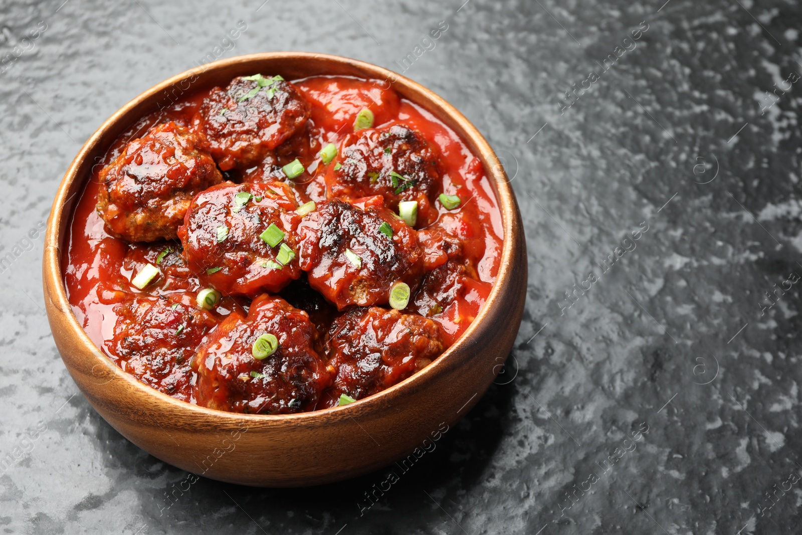 Photo of Delicious meatballs with tomato sauce and herbs on black table, closeup. Space for text