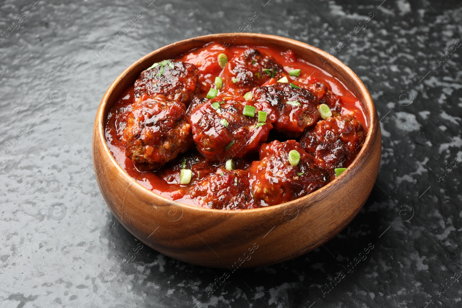 Photo of Delicious meatballs with tomato sauce and herbs on black table, closeup