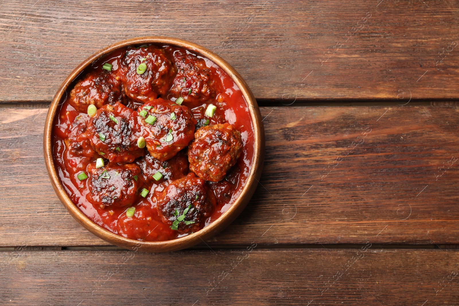 Photo of Delicious meatballs with tomato sauce and herbs on wooden table, top view. Space for text