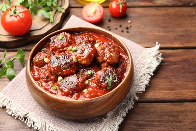 Photo of Delicious meatballs with tomato sauce and herbs served on wooden table, closeup