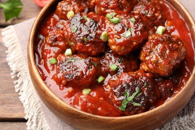 Photo of Delicious meatballs with tomato sauce and herbs on wooden table, closeup