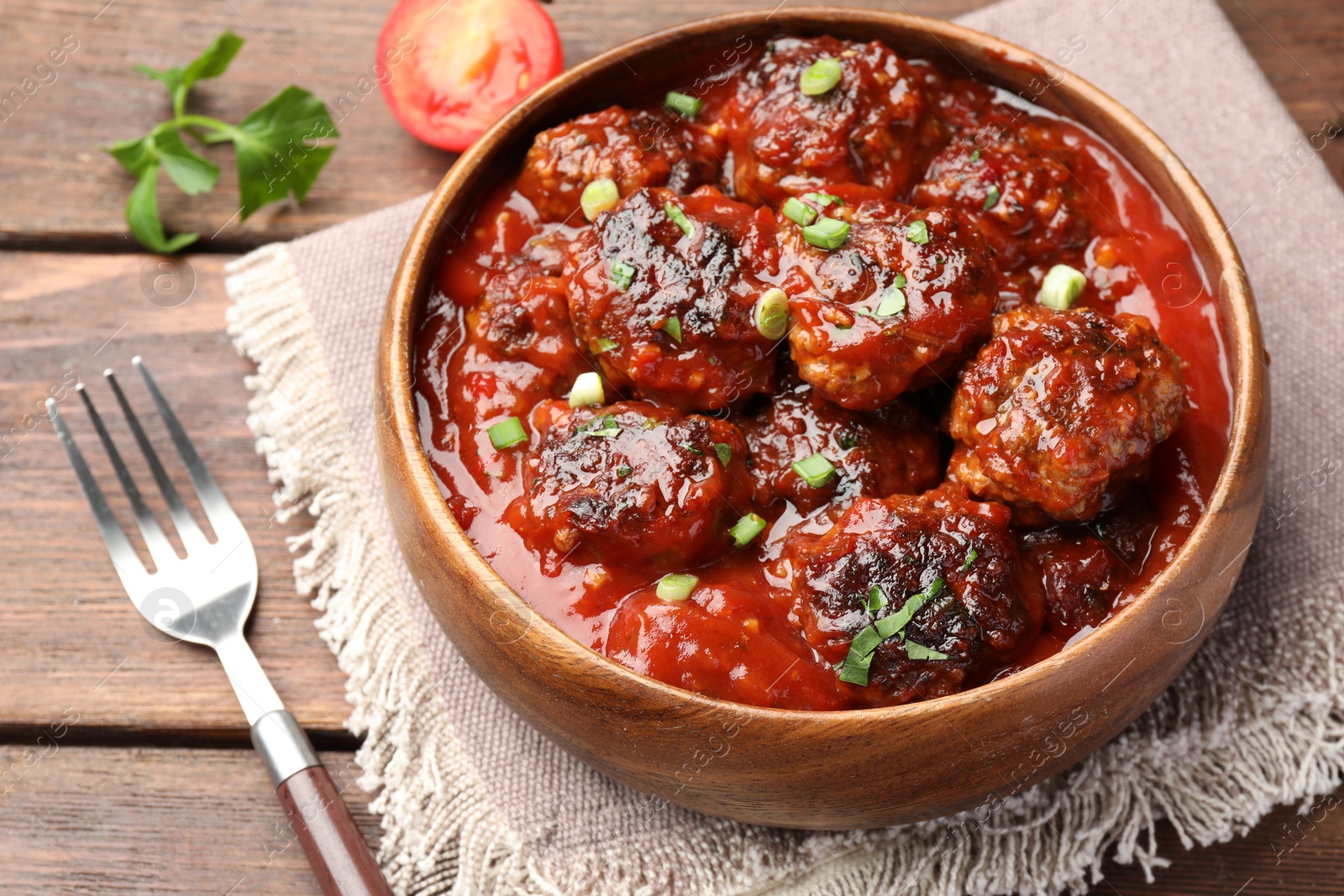 Photo of Delicious meatballs with tomato sauce and herbs served on wooden table, closeup