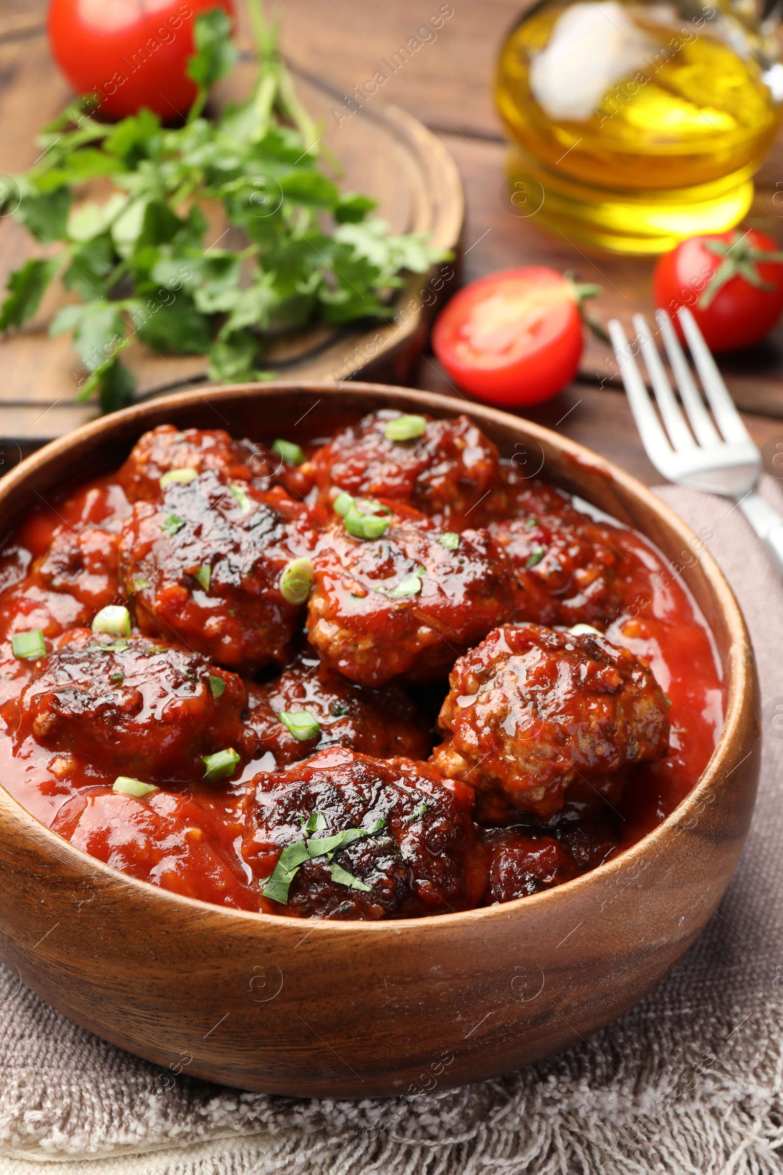 Photo of Delicious meatballs with tomato sauce and herbs served on wooden table, closeup