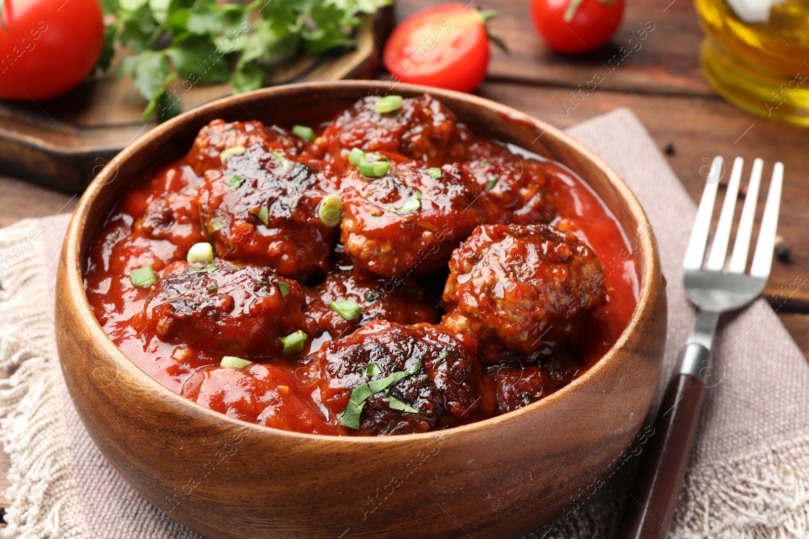 Photo of Delicious meatballs with tomato sauce and herbs served on wooden table, closeup