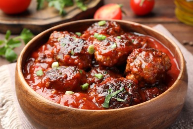 Photo of Delicious meatballs with tomato sauce and herbs on wooden table, closeup