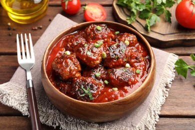 Photo of Delicious meatballs with tomato sauce and herbs served on wooden table, closeup