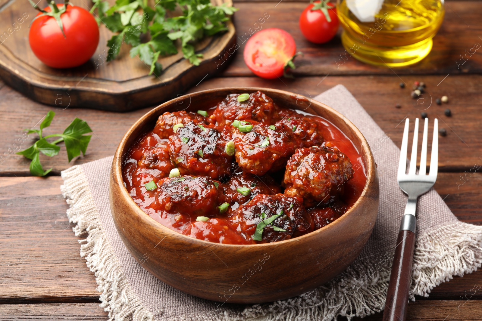 Photo of Delicious meatballs with tomato sauce and herbs served on wooden table, closeup