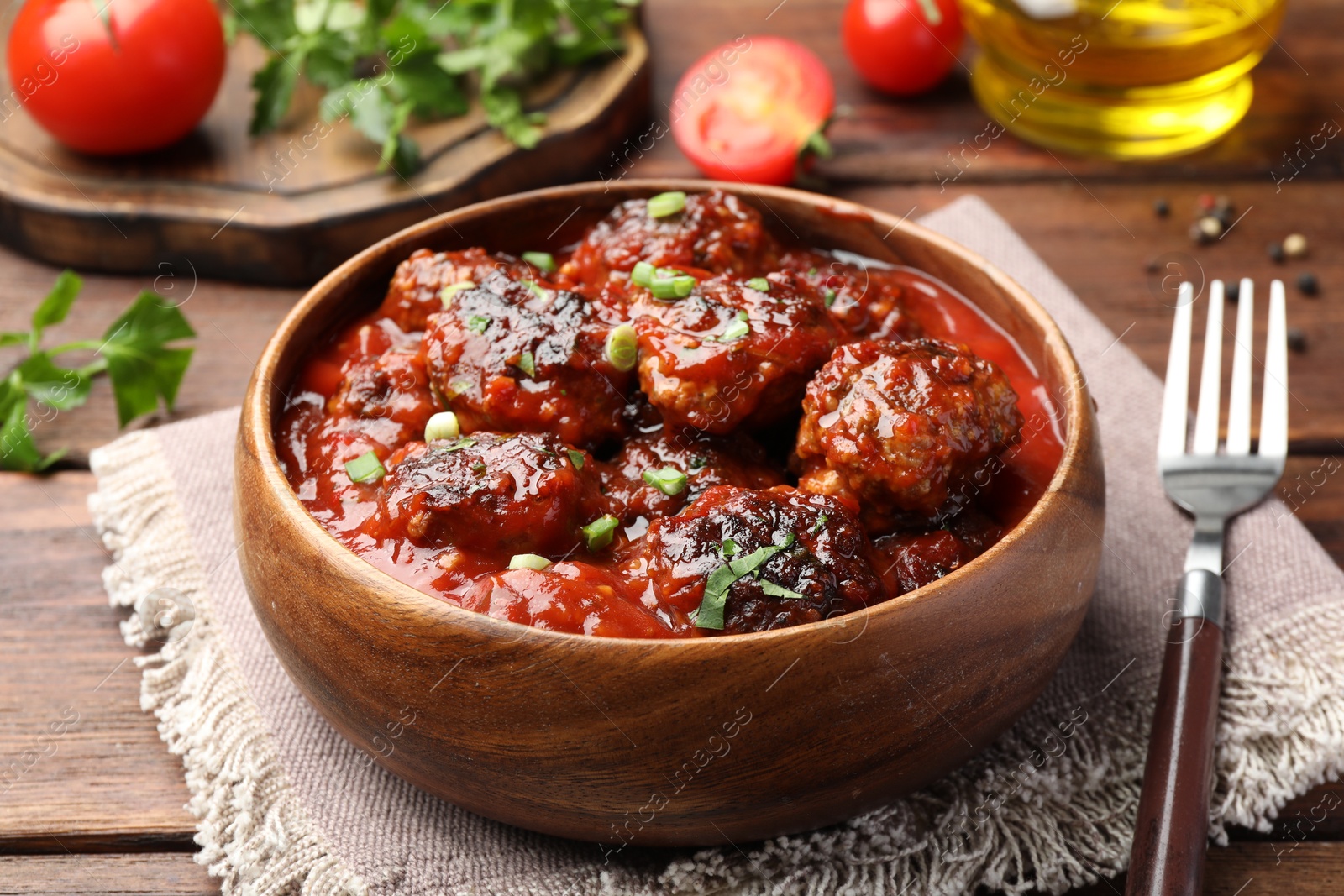 Photo of Delicious meatballs with tomato sauce and herbs served on wooden table, closeup