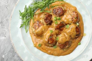 Photo of Delicious meatballs with gravy cream sauce, herbs and arugula on grey table, top view