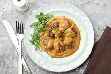 Photo of Delicious meatballs with gravy cream sauce, herbs and arugula served on grey table, flat lay