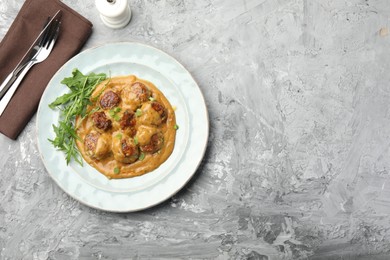 Photo of Delicious meatballs with gravy cream sauce, herbs and arugula served on grey table, flat lay. Space for text