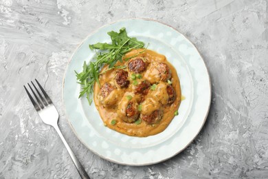 Photo of Delicious meatballs with gravy cream sauce, herbs and arugula served on grey table, top view