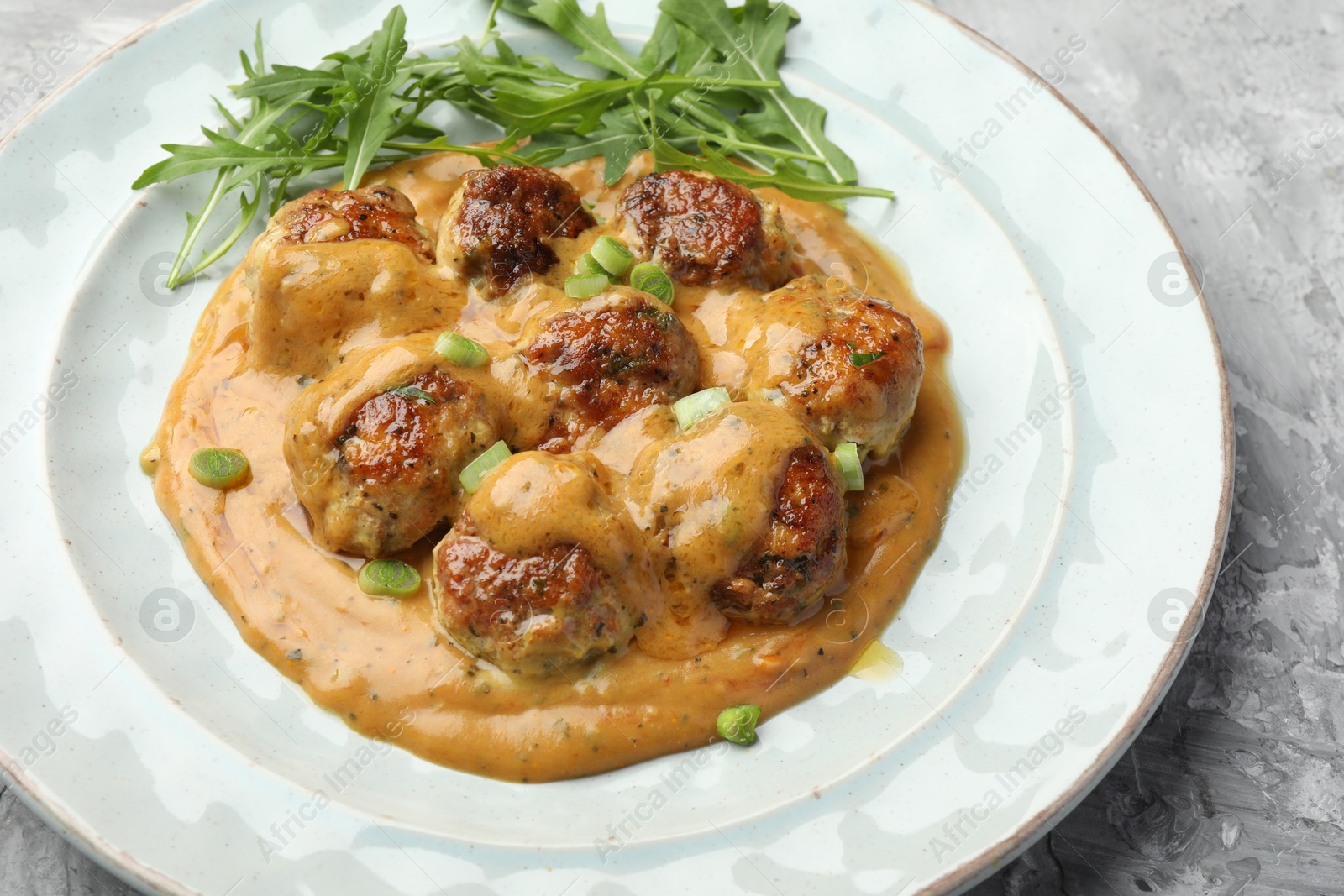 Photo of Delicious meatballs with gravy cream sauce, herbs and arugula on grey table, closeup