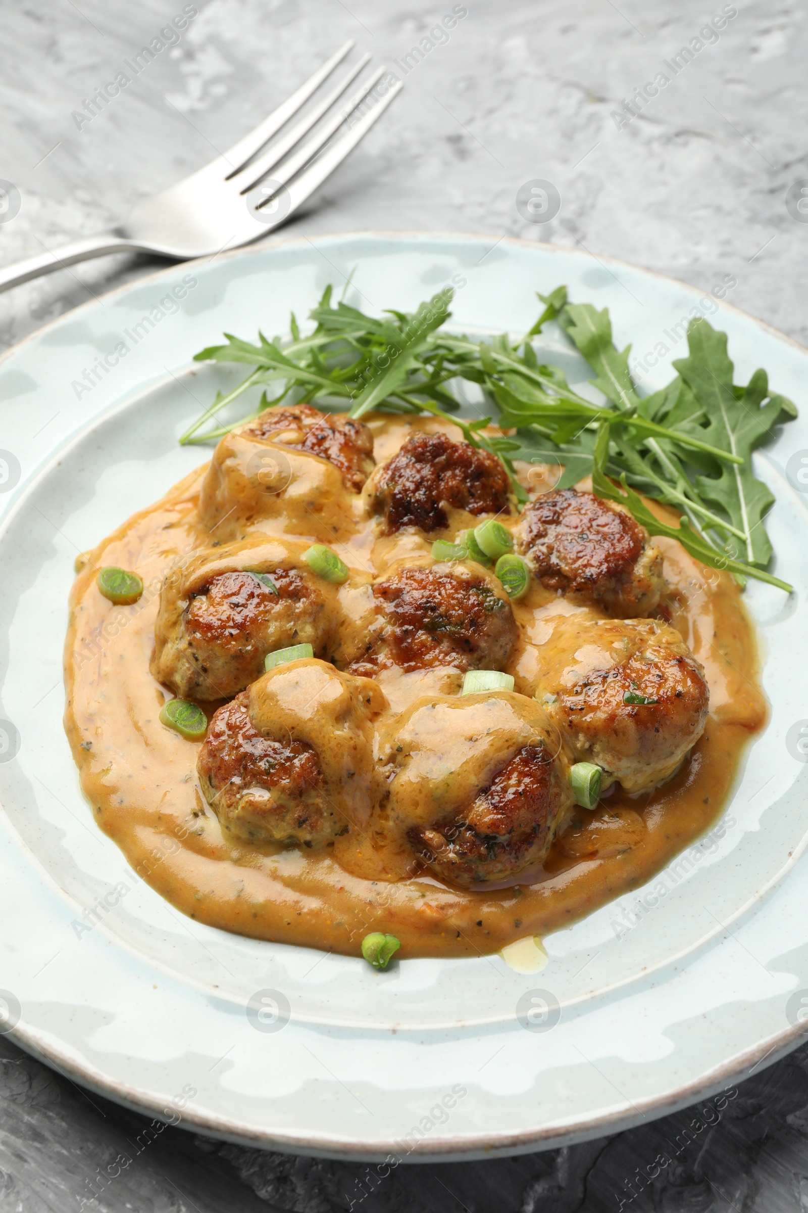 Photo of Delicious meatballs with gravy cream sauce, herbs and arugula served on grey table, closeup