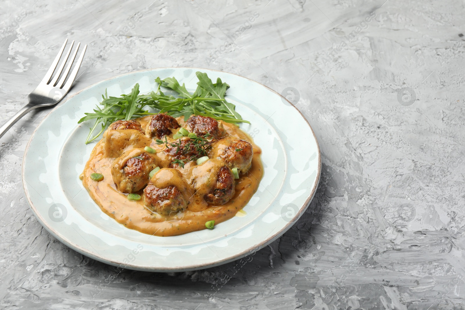 Photo of Delicious meatballs with gravy cream sauce, herbs and arugula served on grey table. Space for text