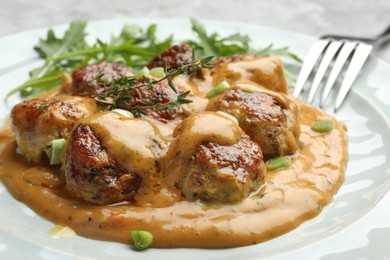 Photo of Delicious meatballs with gravy cream sauce, herbs and arugula served on table, closeup