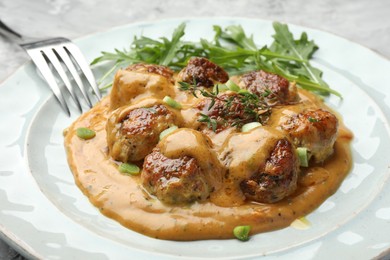 Photo of Delicious meatballs with gravy cream sauce, herbs and arugula served on table, closeup