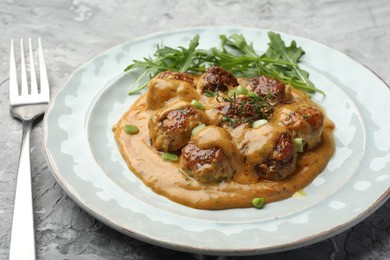 Photo of Delicious meatballs with gravy cream sauce, herbs and arugula served on grey table, closeup