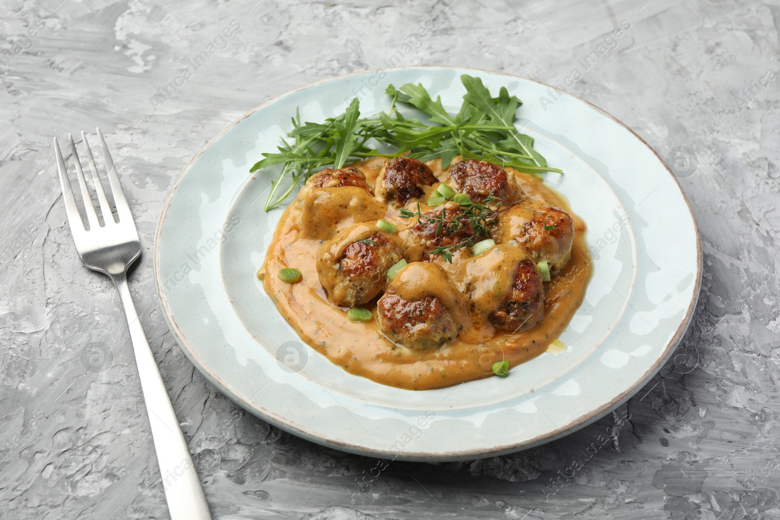 Photo of Delicious meatballs with gravy cream sauce, herbs and arugula served on grey table