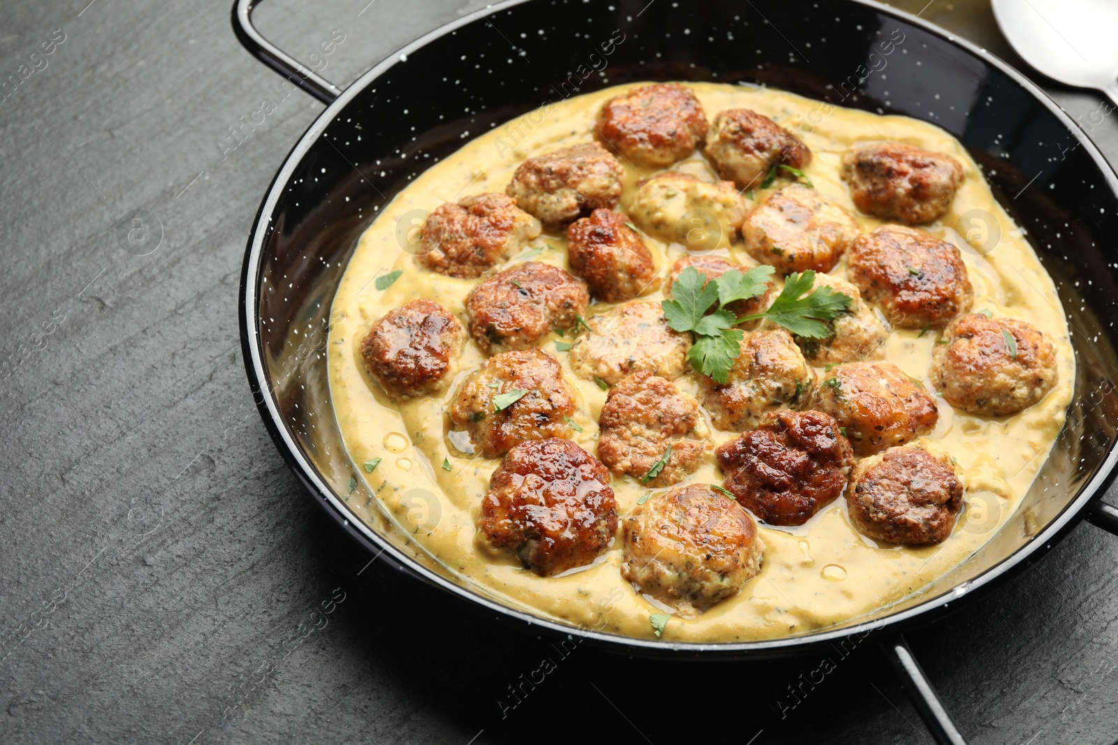 Photo of Delicious meatballs with gravy cream sauce and herbs on black table, closeup