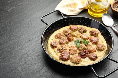 Photo of Delicious meatballs with gravy cream sauce and herbs served on black table. Space for text