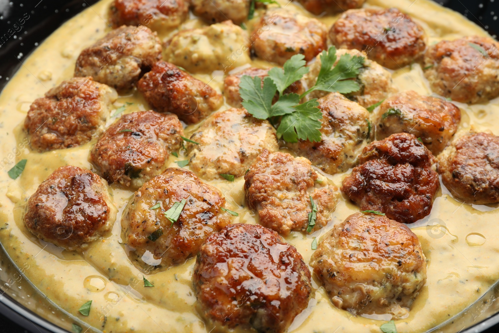 Photo of Delicious meatballs with gravy cream sauce and herbs in pan, closeup