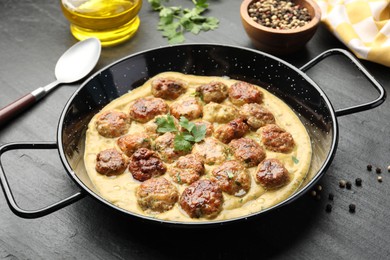 Photo of Delicious meatballs with gravy cream sauce and herbs served on black table, closeup