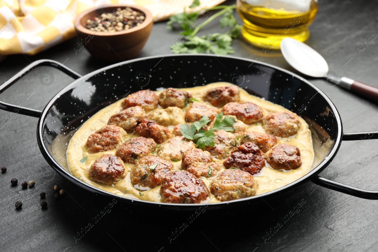 Photo of Delicious meatballs with gravy cream sauce and herbs served on black table, closeup