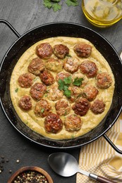 Photo of Delicious meatballs with gravy cream sauce and herbs served on black table, flat lay