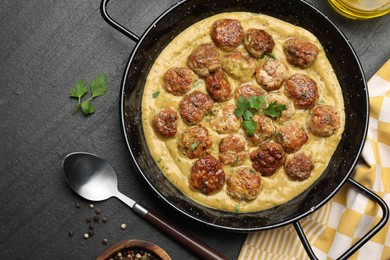 Photo of Delicious meatballs with gravy cream sauce and herbs served on black table, flat lay