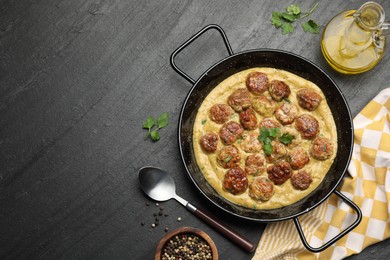 Photo of Delicious meatballs with gravy cream sauce and herbs served on black table, flat lay. Space for text