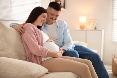 Photo of Pregnant woman and her husband on sofa at home