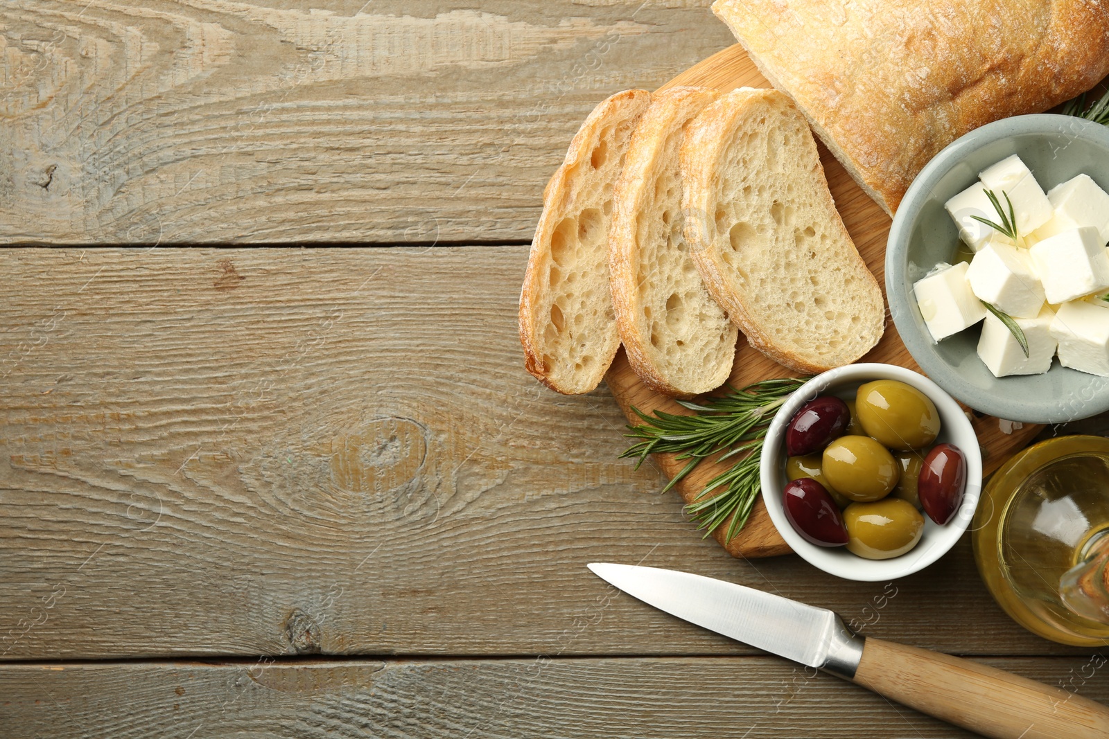 Photo of Delicious marinated olives, bread and feta cheese served on wooden table, top view. Space for text